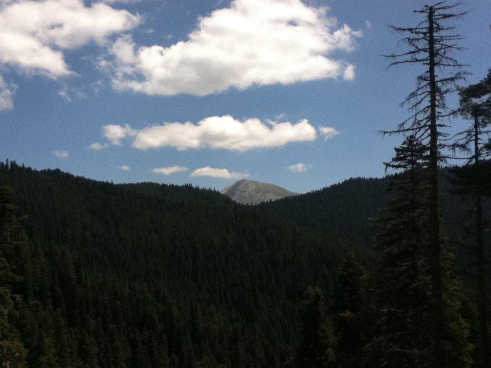 Clouds above a mountain with a valley of forests in front of it.